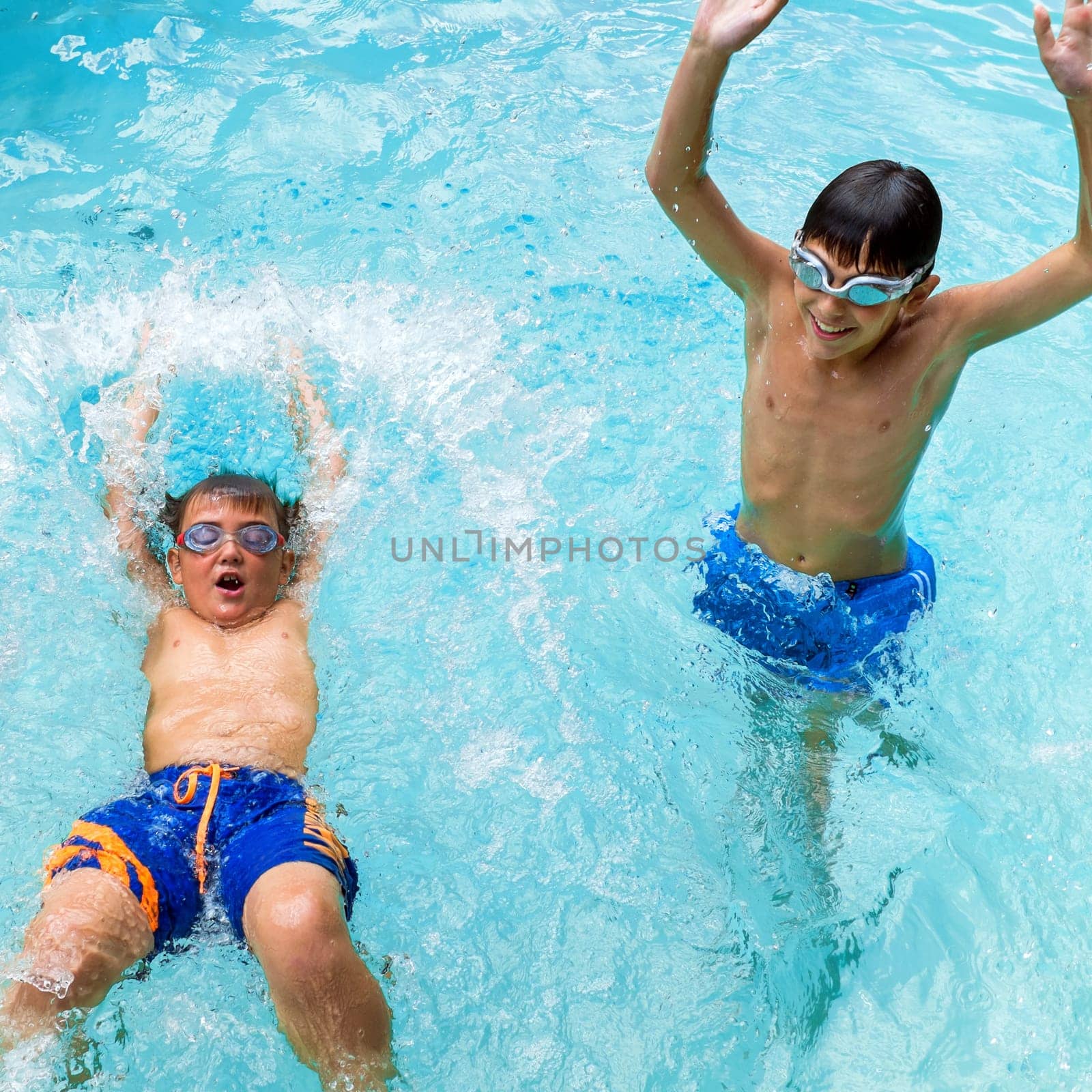 Portrait of two boys splashing water together in pool.
