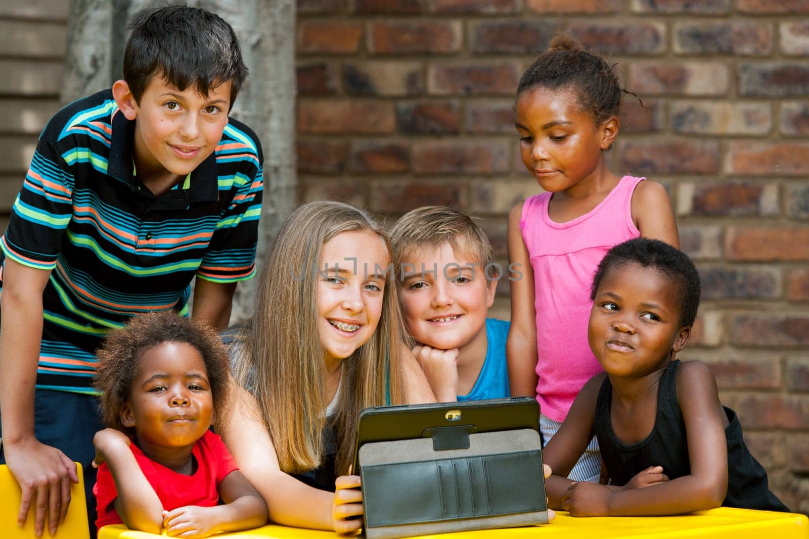 Group of diverse kids playing together on digital tablet outdoors.