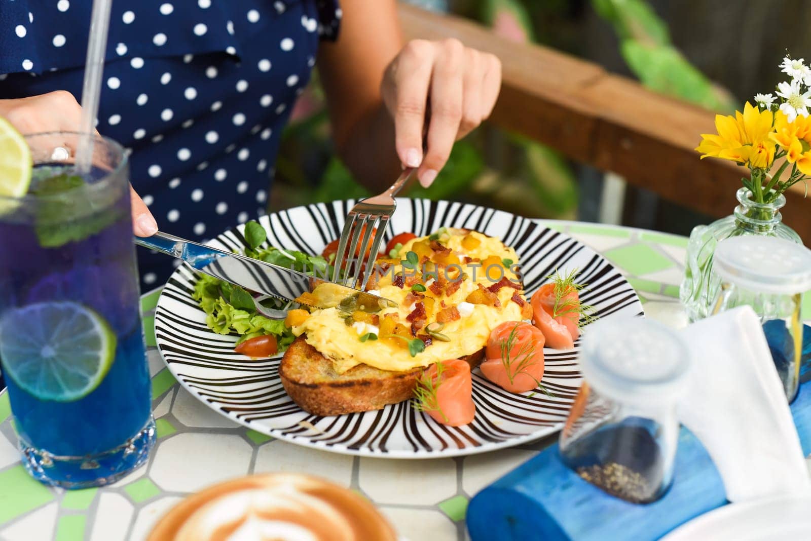 Woman holding knife and fork cutting toast with scrambled eggs pumpkin puree and cubes, smoked salmon and pumpkin seeds