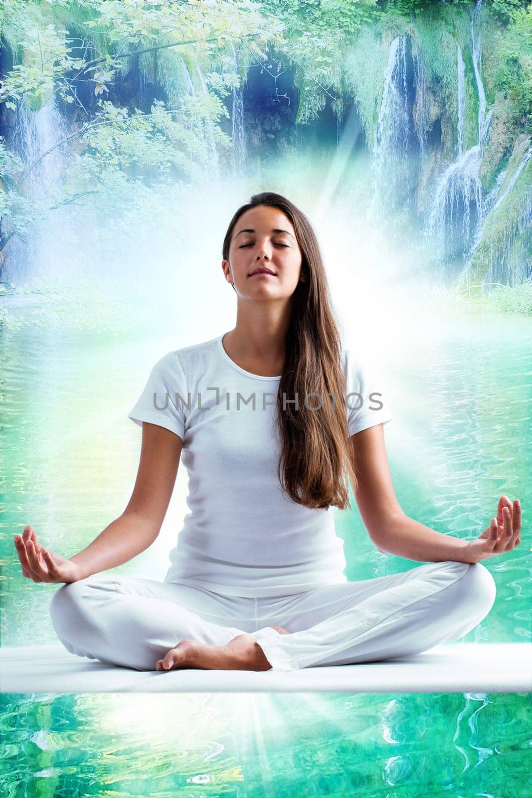Close up portrait of attractive woman dressed in white meditating. Young girl sitting i yoga position at mystic blue lagoon with waterfalls in background.