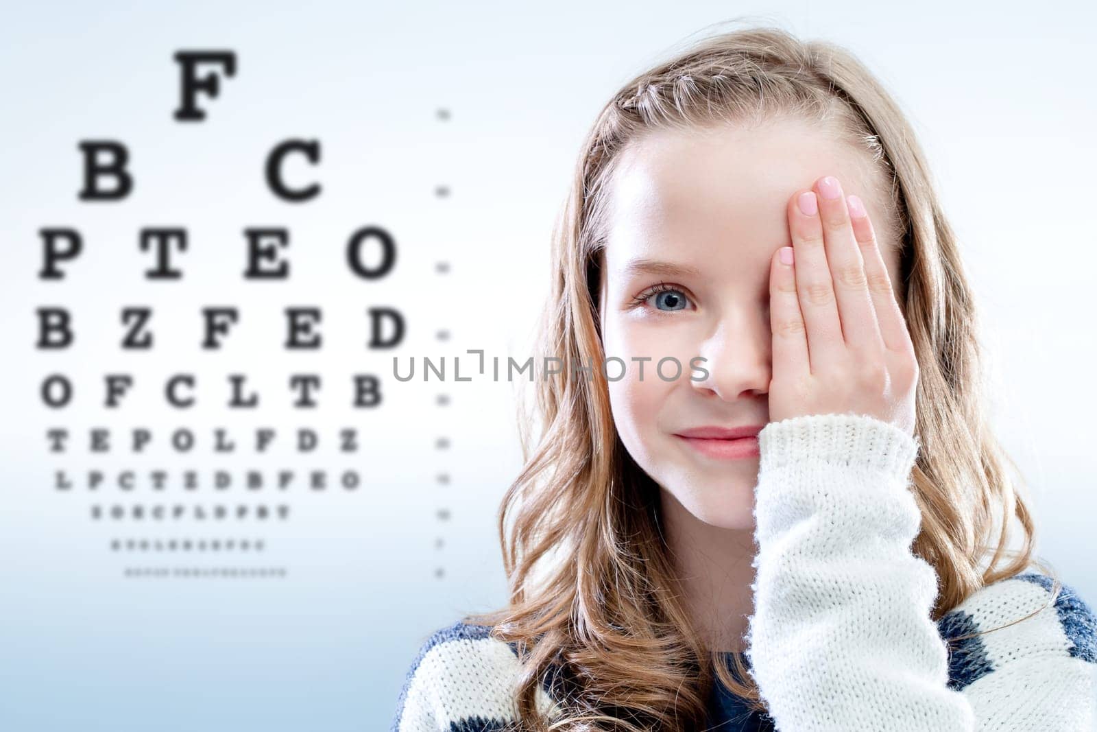 Close up portrait of girl reviewing eyesight closing eye with hand.Out of focus test chart in background.