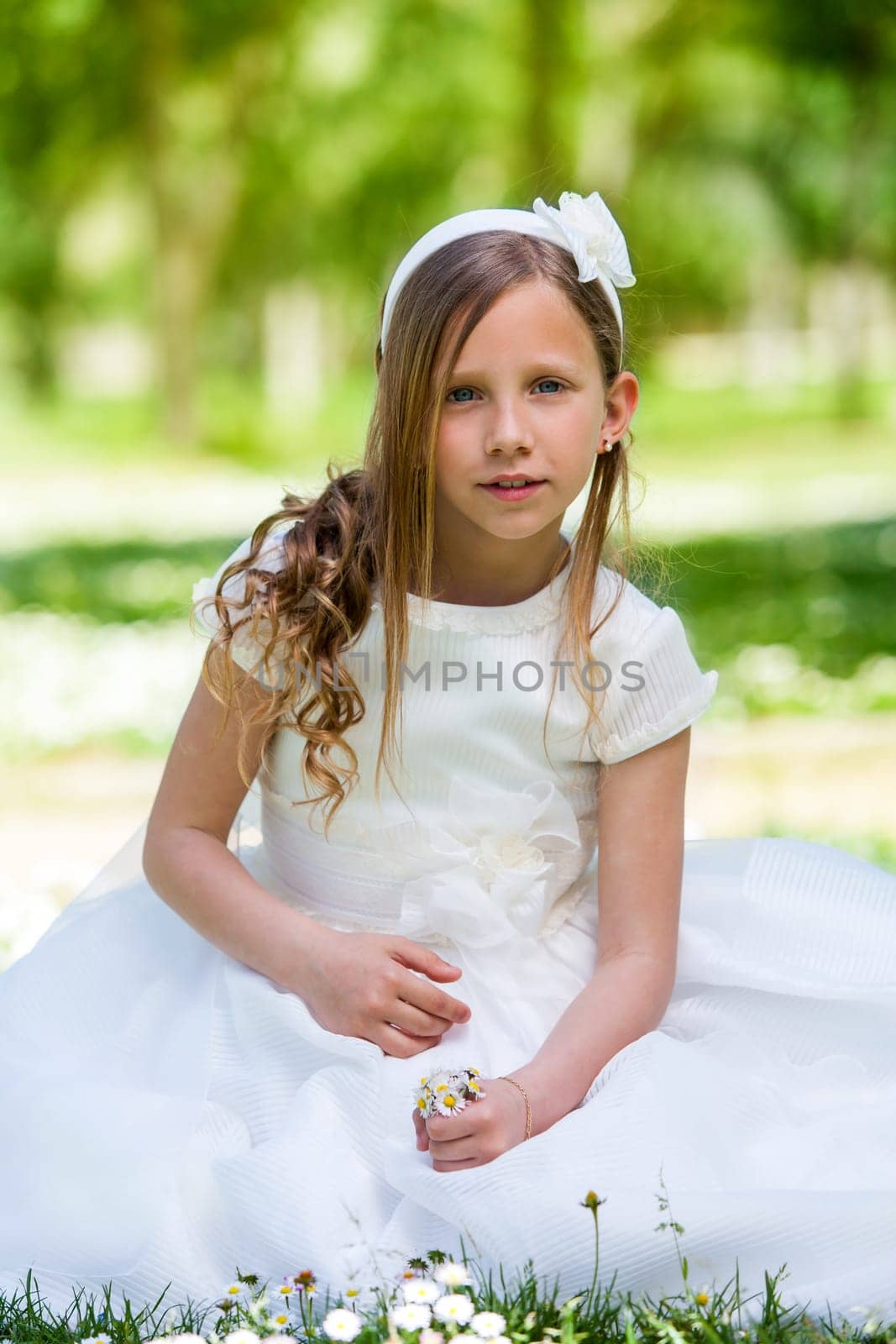 Portrait of cute girl in communion dress holding flowers outdoors.