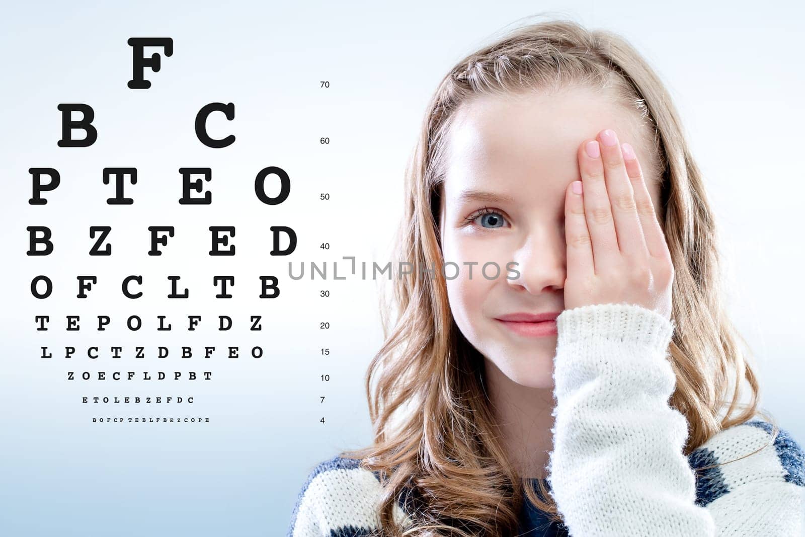 Close up portrait of Girl reviewing eye sight closing eye with hand.Test chart in background.