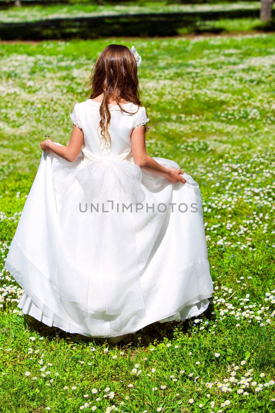 Young girl in white dress walking in flower field.