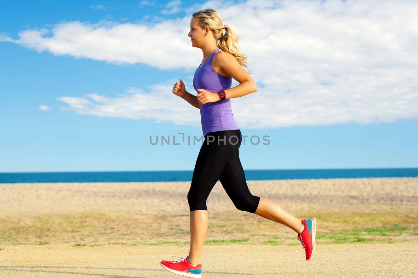 Close up motion portrait of attractive young girl jogging along beach at late afternoon.
