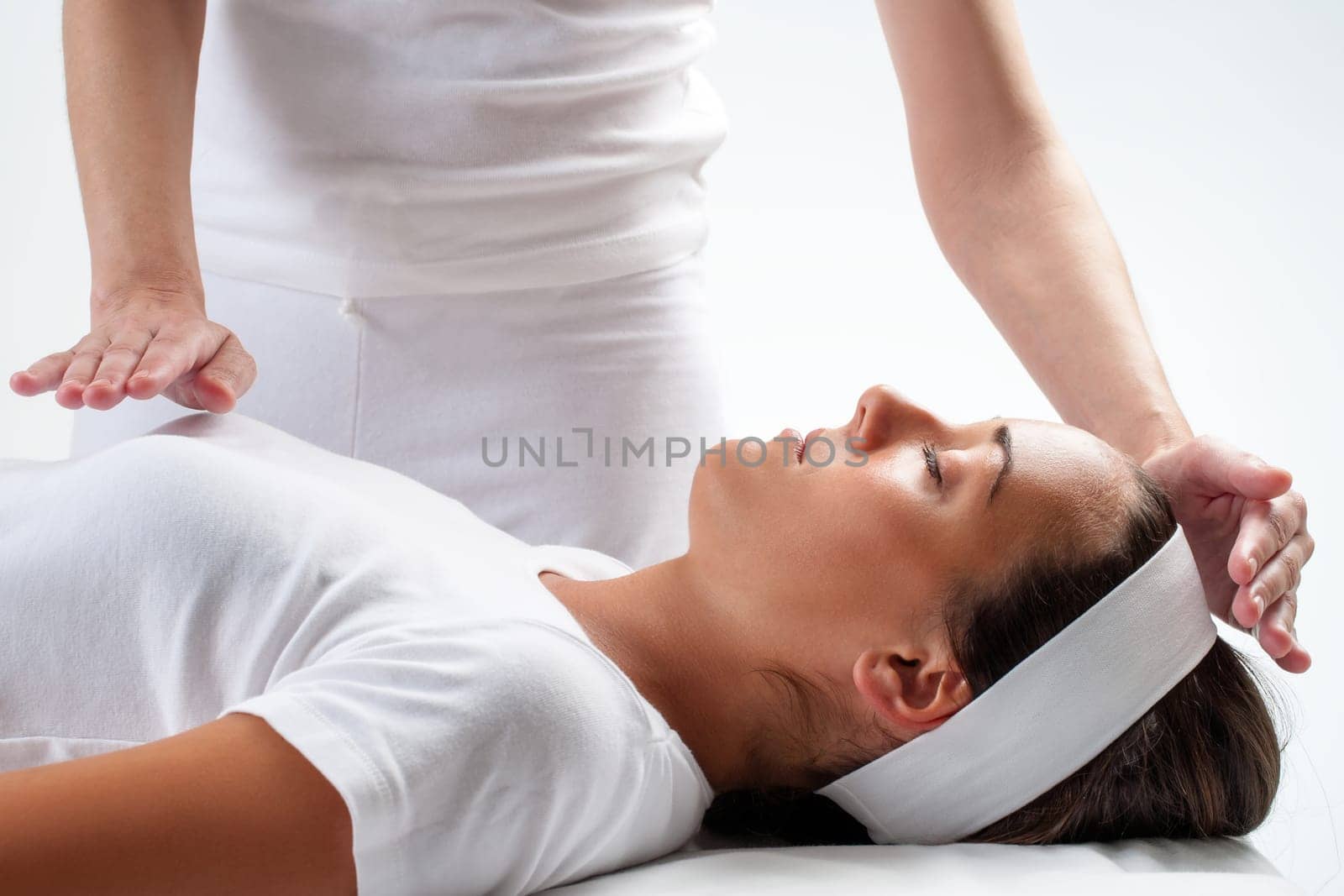 Close up of chiropractor’s hands doing reiki on young woman.One hand on head and one hand on chest.