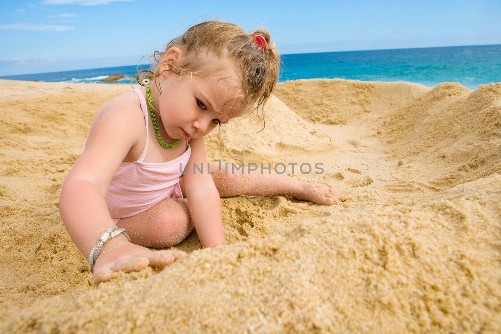 Baby girl playing with sand on the beach, Cabo San Lucas, Mexico