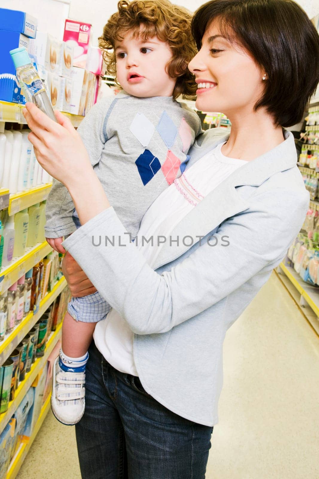 Woman carrying her son and choosing a baby oil in a supermarket