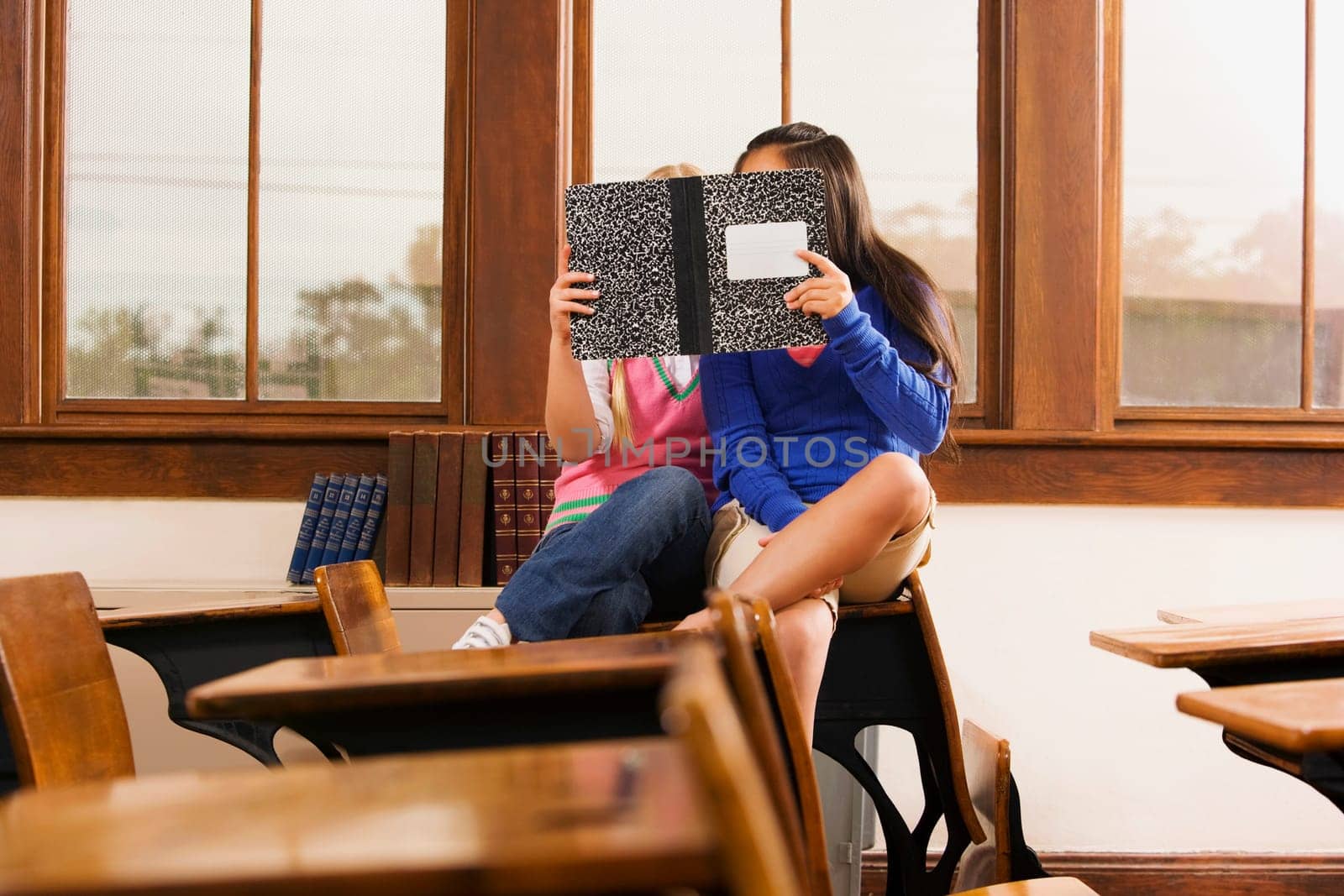Two schoolgirls reading a book in a classroom
