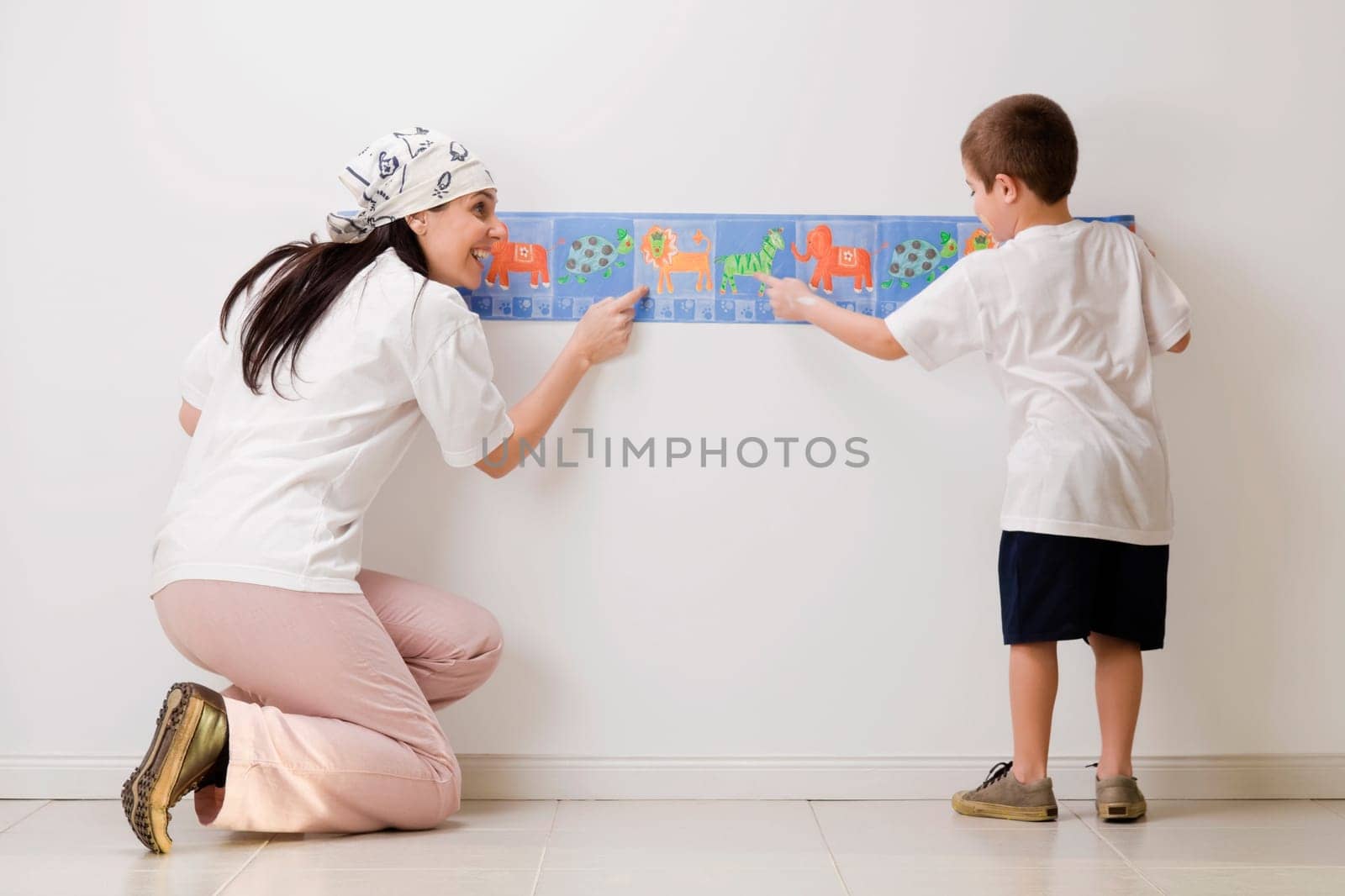 Rear view of a boy and his mother pasting wallpaper on the wall