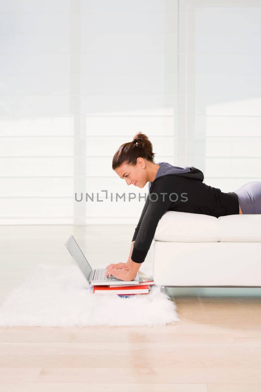 Side profile of a young woman lying on the bed and using a laptop