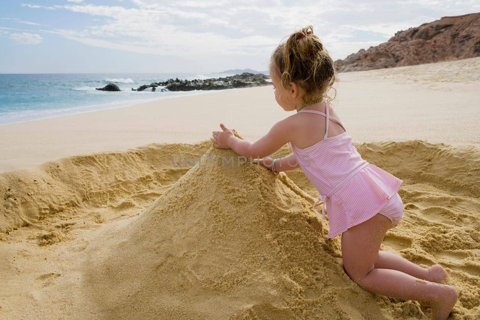 Baby girl playing with sand on the beach, Cabo San Lucas, Mexico