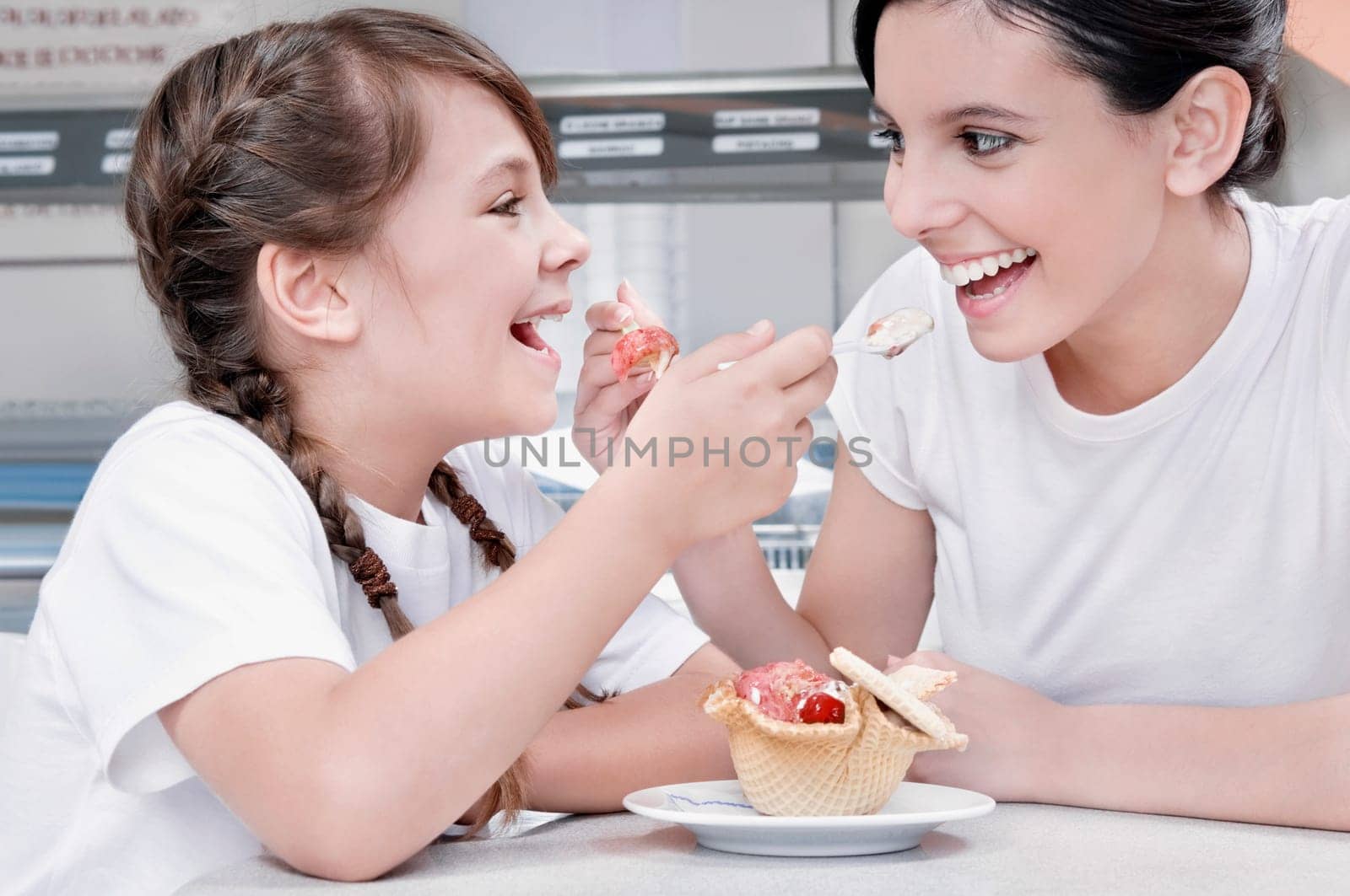 Girl and a teenage girl feeding ice cream to each other