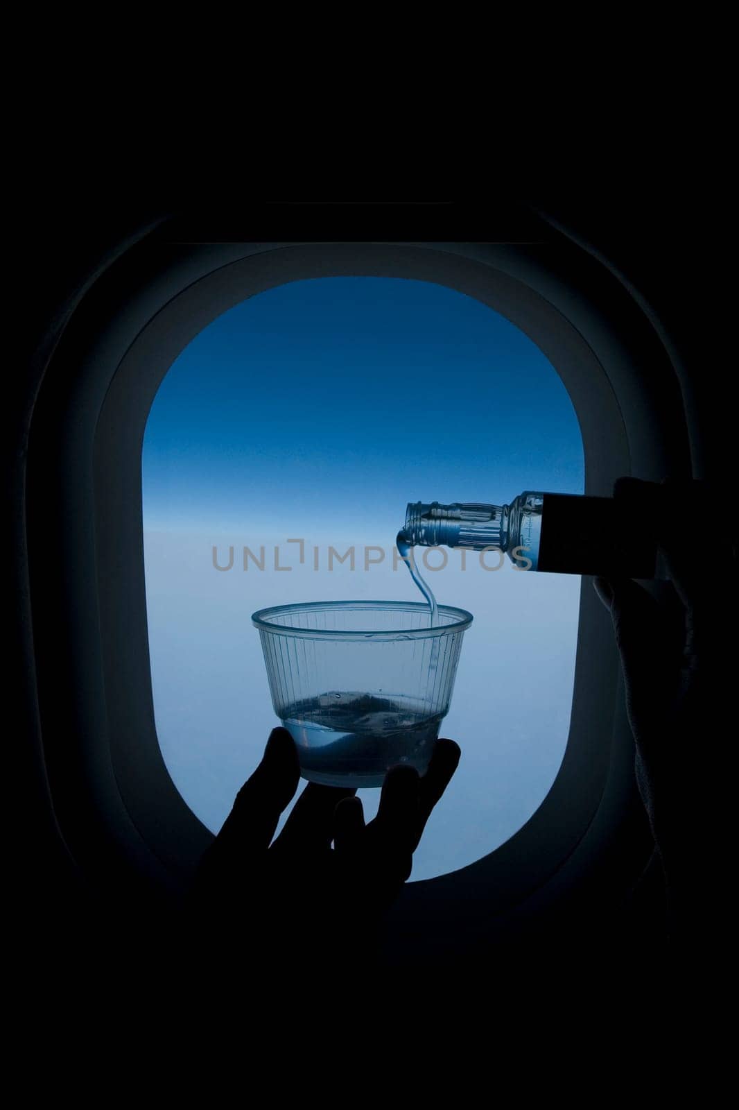 Person pouring whiskey into a glass in front of an airplane window