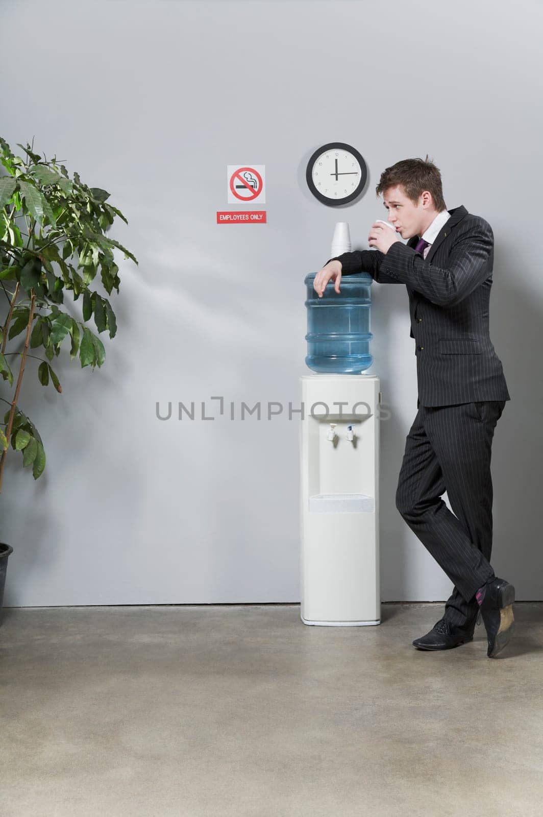 Businessman leaning on a water cooler and drinking water