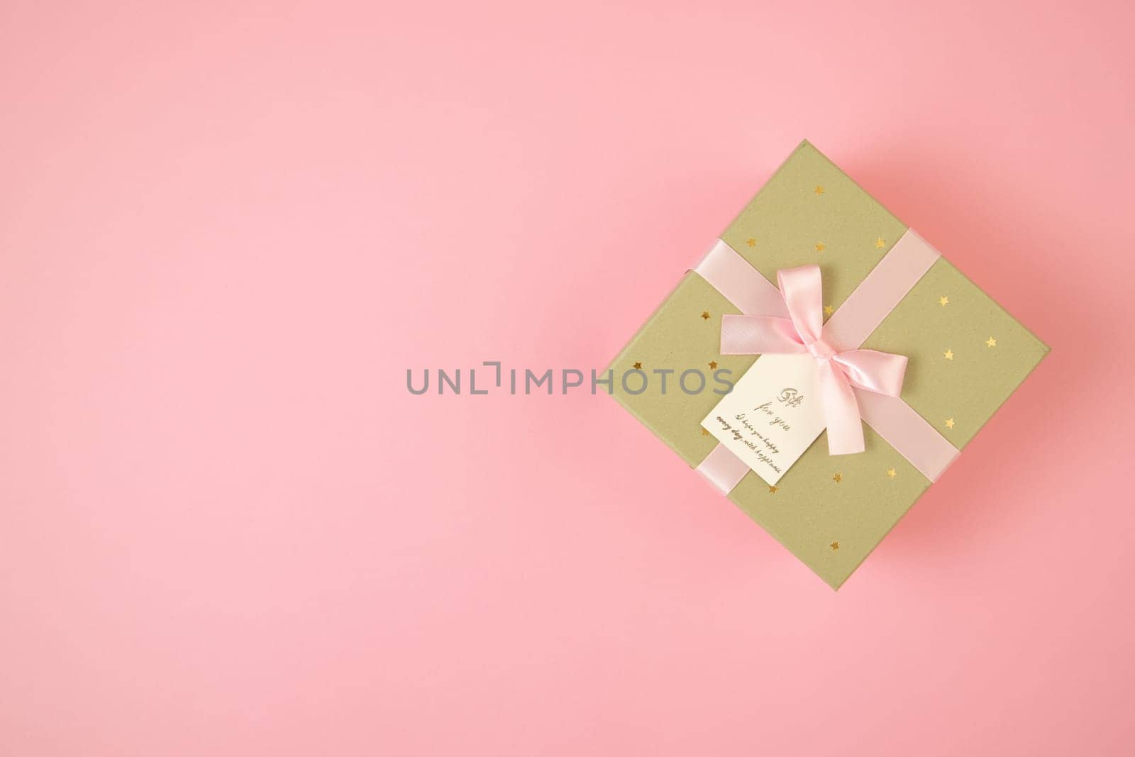 Golden box with ribbon lying on pink background with copy space. Wrapped gift on table with space for text. Valentine s present in flat lay composition.