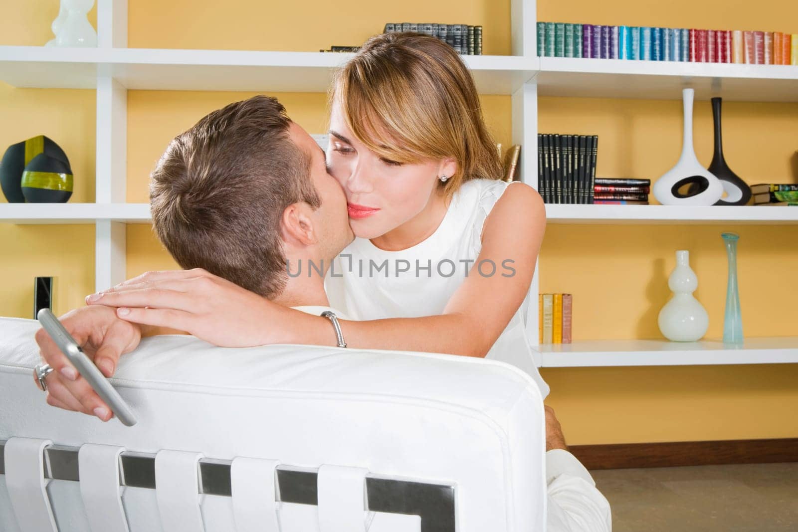 Young couple kissing each other and young woman holding a mobile phone