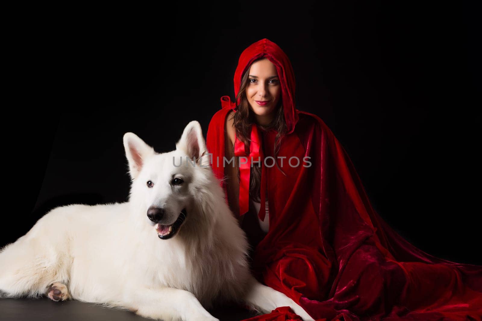 Woman wearing a red hood posing in studio with her dog