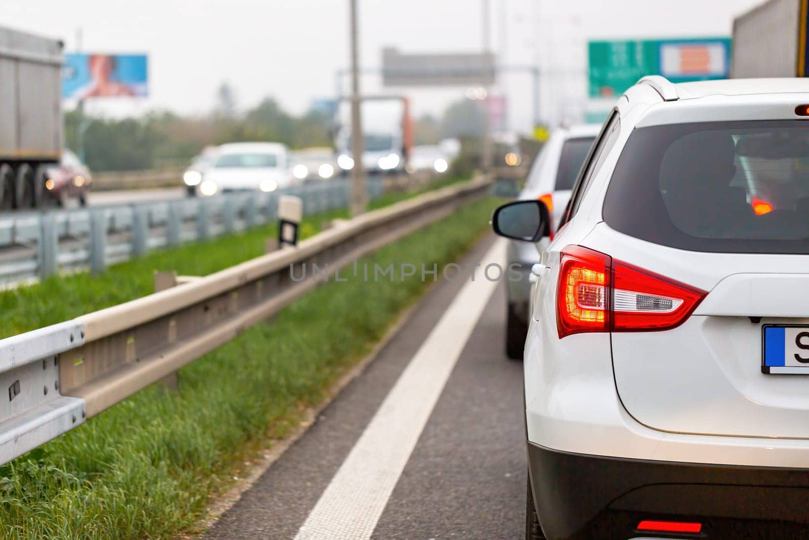 White car waiting in traffic jam on highway in rush hour. Automobile stuck on crowded road in evening. Vehicles in line with illuminated brake lights on full street.