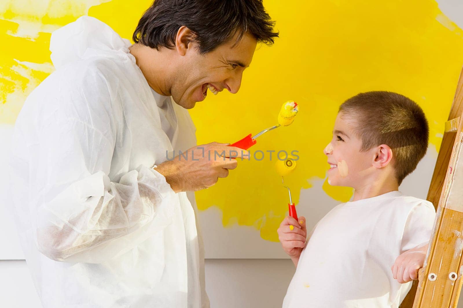 Mid adult man with his son holding paint rollers and looking at each other