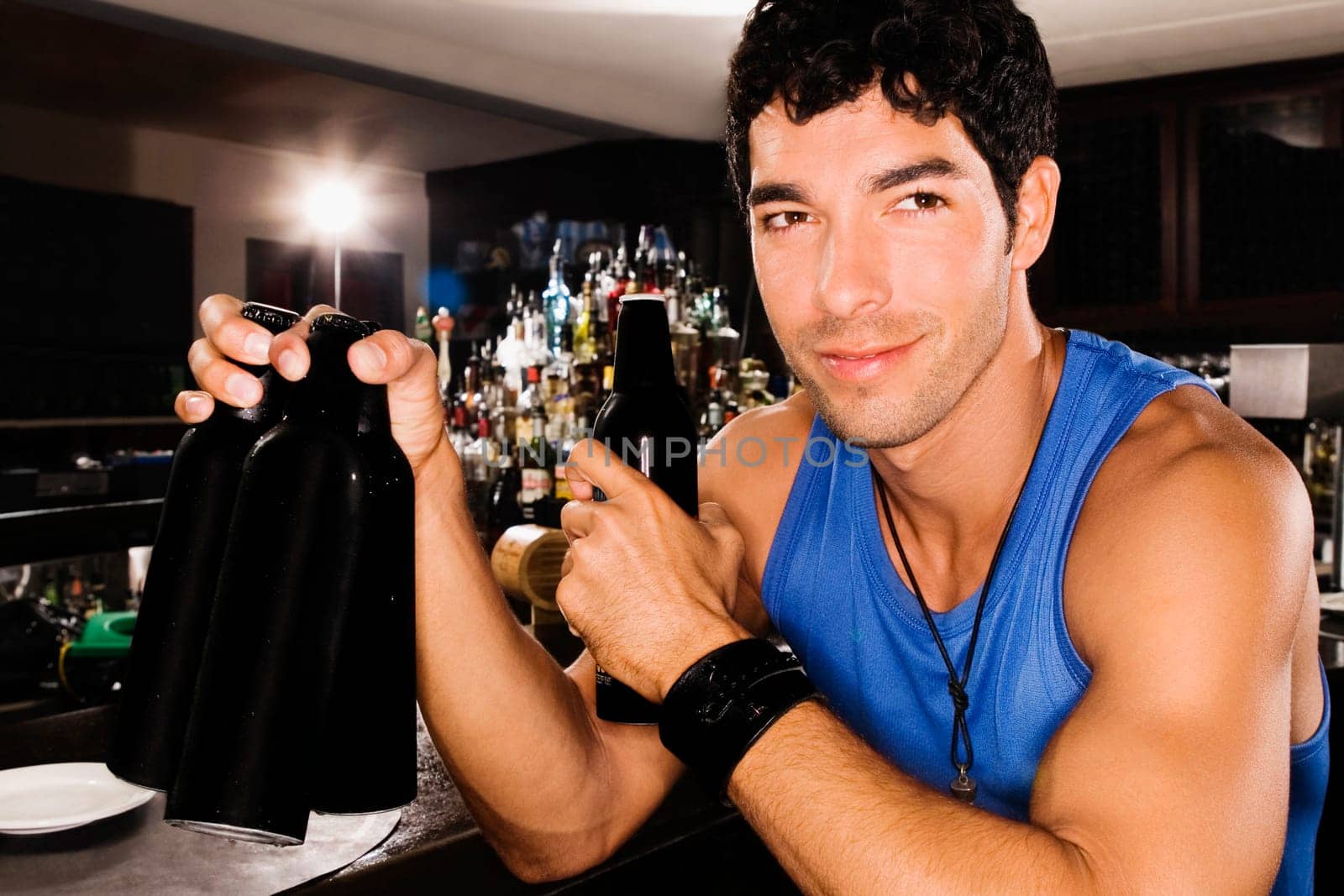 Close_up of a young man sitting at a bar counter and holding beer bottles
