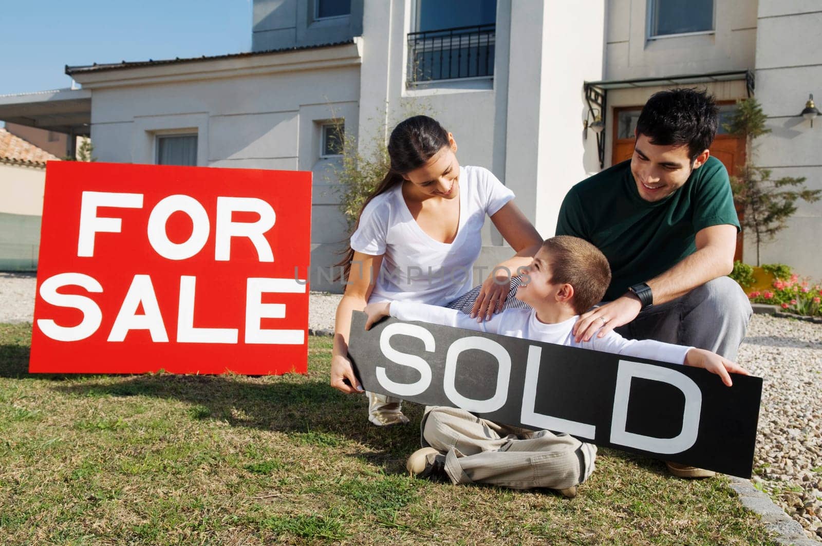 Young couple with their son sitting near for sale information board and smiling