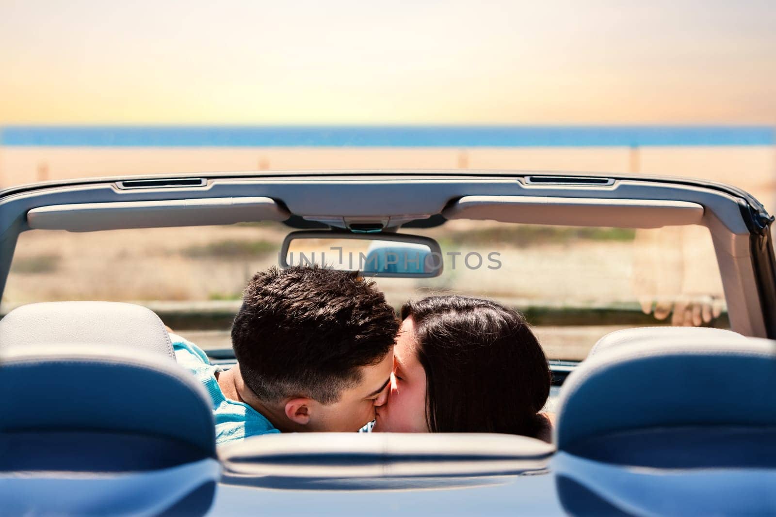 Portrait of young couple kissing in convertible. Rear view of couple in car next to beach.
