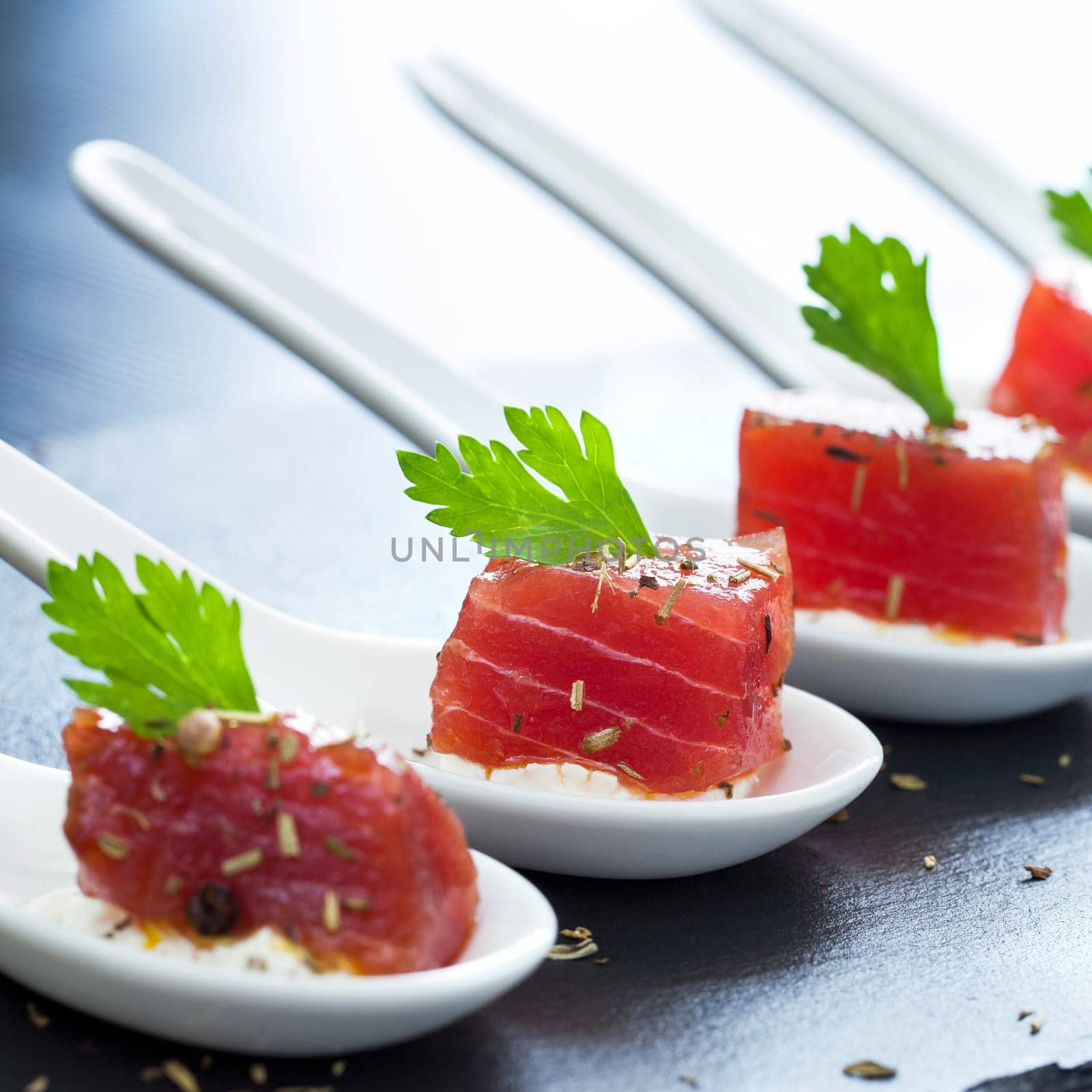 Extreme close up of multiple appetizing tuna dices on white ceramic spoons.