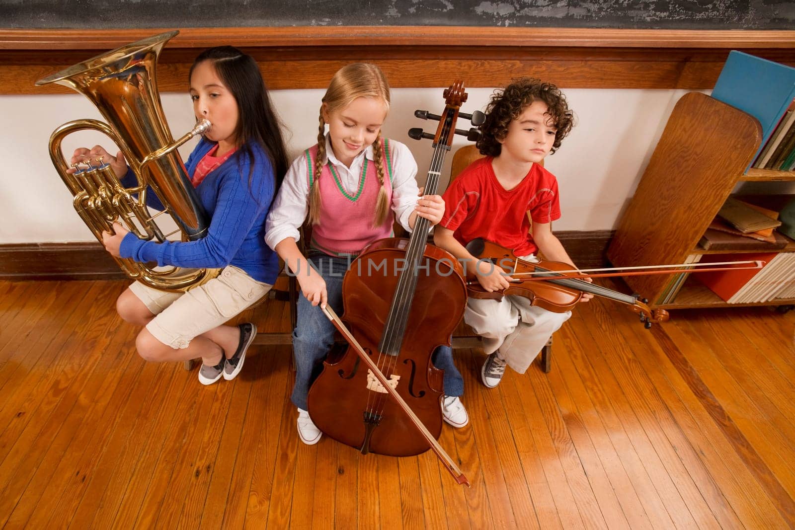 Three students playing musical instruments in a classroom