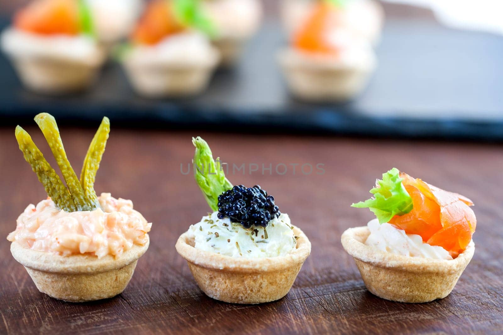 Macro close up of three Mini puff open pastry tartlets topped with different seafood fillings. Tartlet platter out of focus in background with copy space..