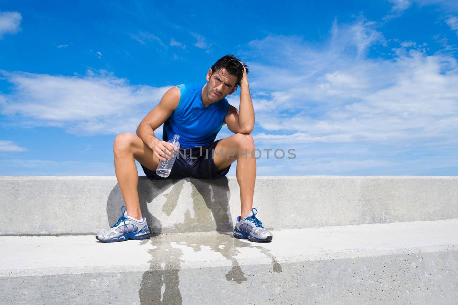 Young man sitting on a ledge and holding a water bottle
