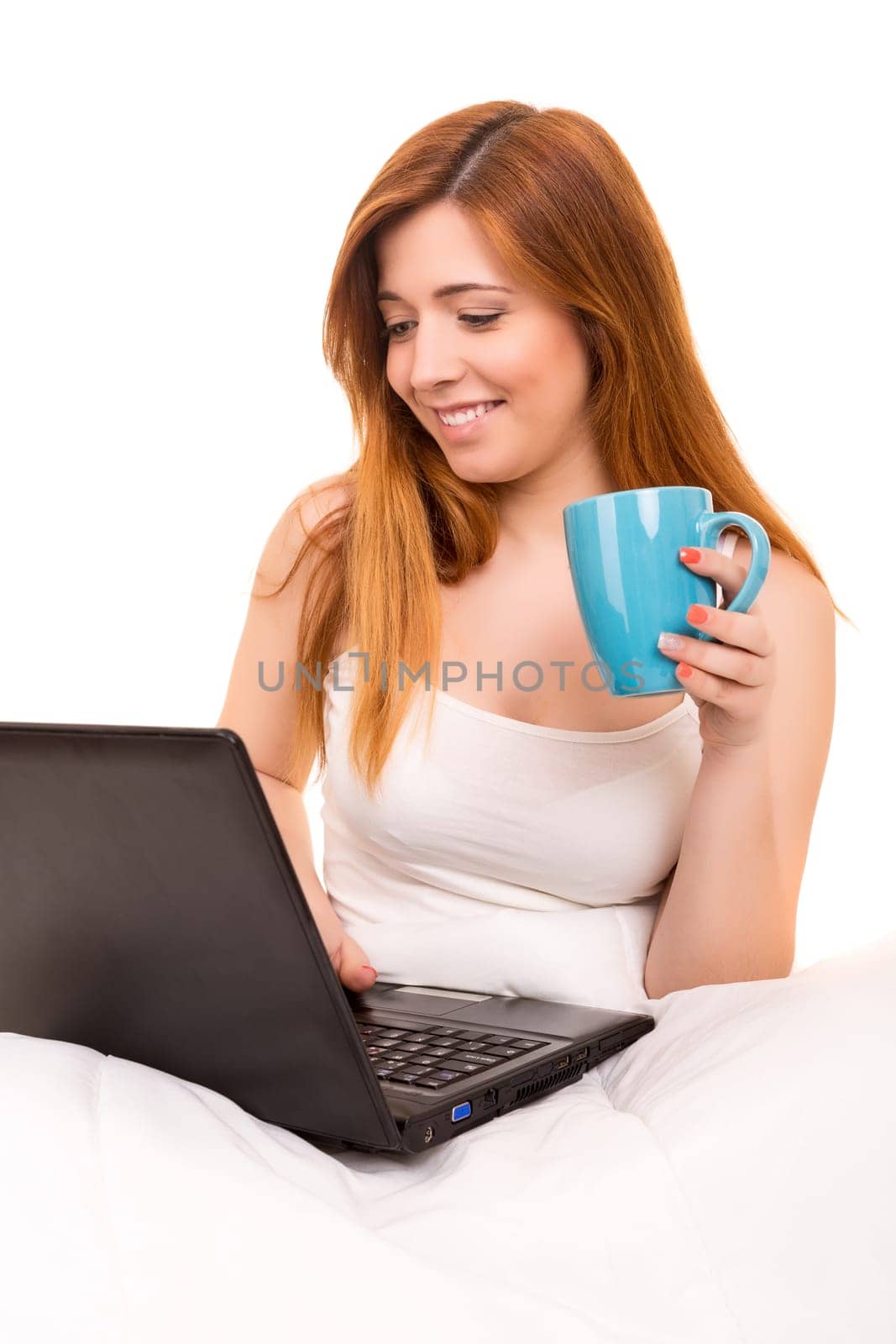 Young beautiful woman having breakfast in bed while working or relaxing with her computer