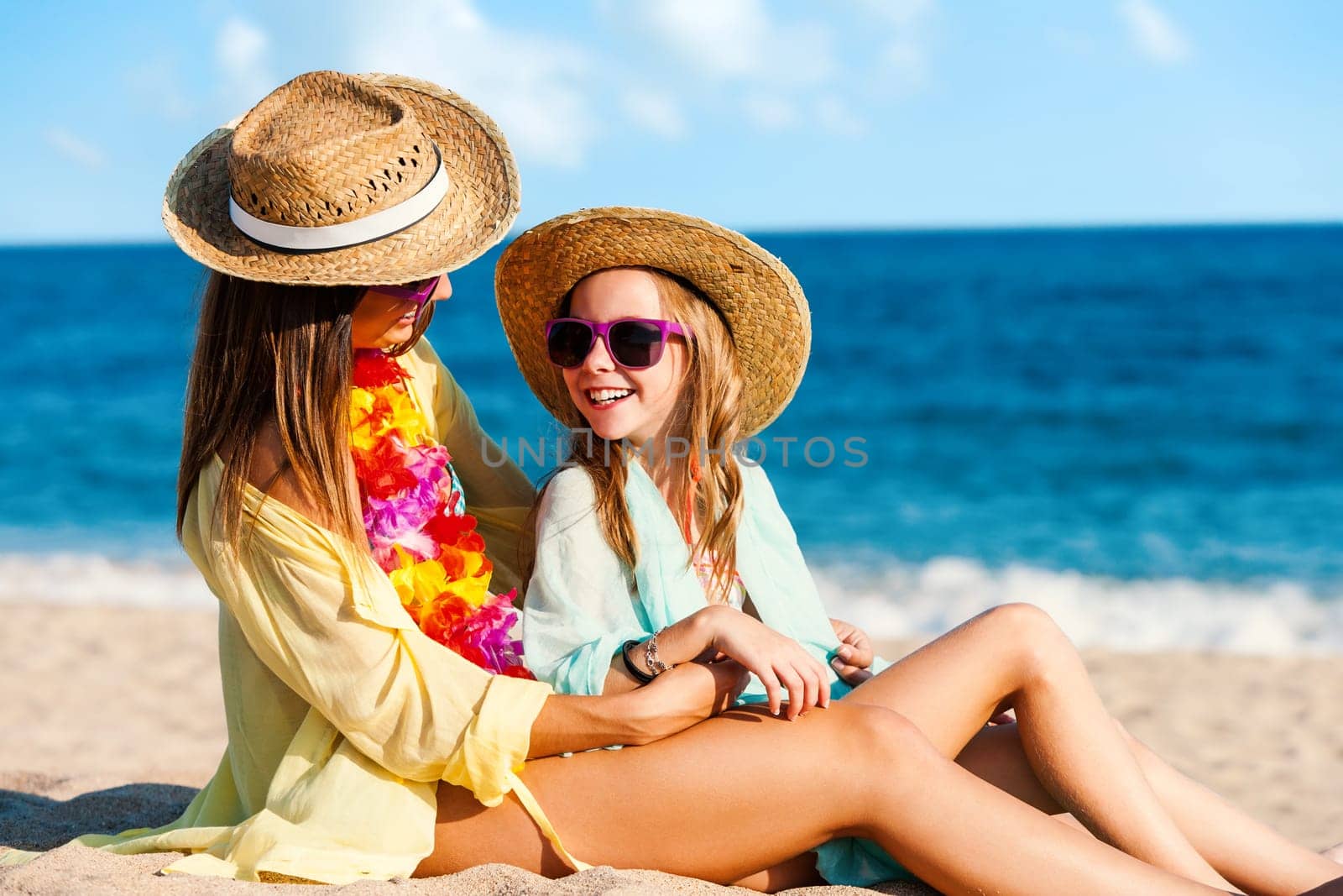 Close up portrait of young mother and daughter on summer holidays. Two young women in swimwear with straw hats and fun purple sunglasses.