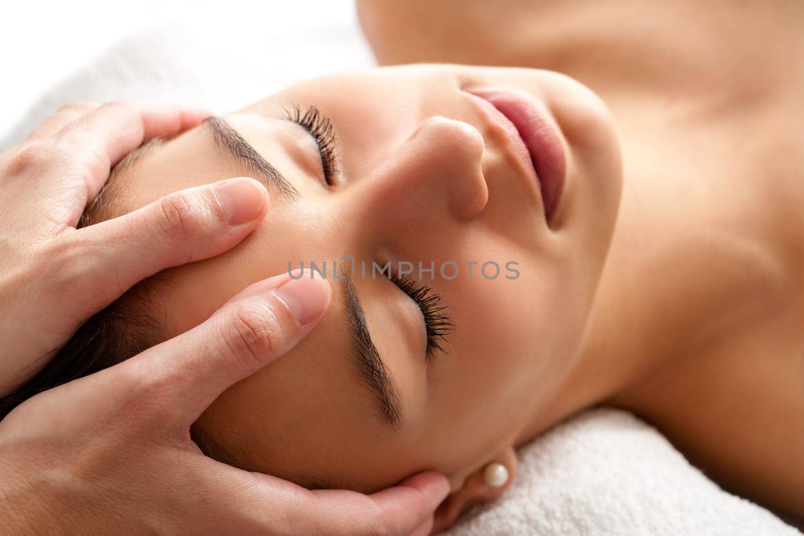 Close up head shot  of Woman having curative facial massage. Therapist applying pressure with thumbs on forehead.