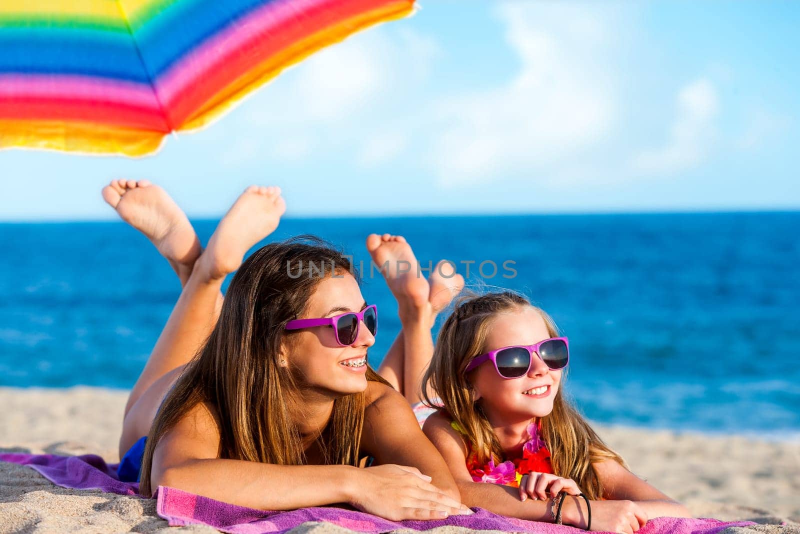 Close up portrait of two young girls laying together on beach..Young women wearing fun purple eyewear..