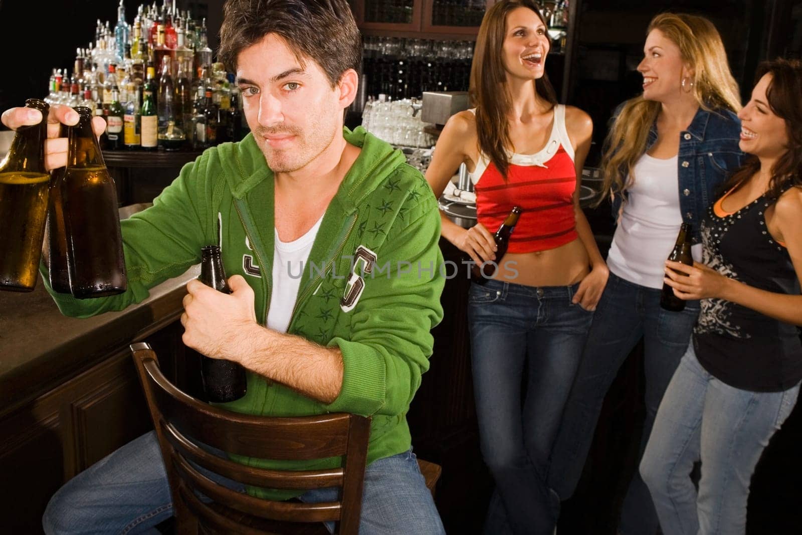 Portrait of a young man holding beer bottles at a bar counter with his three friends standing behind him