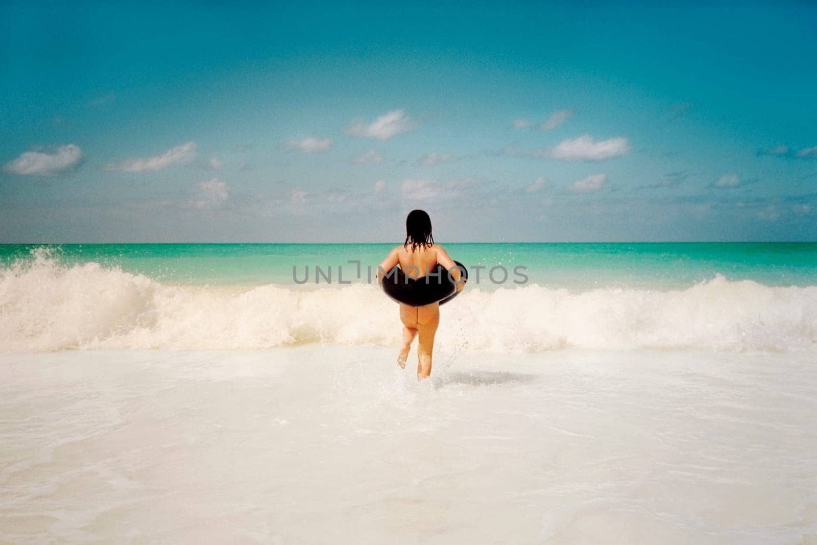 Rear view of a naked woman wearing an inflatable ring and walking in water