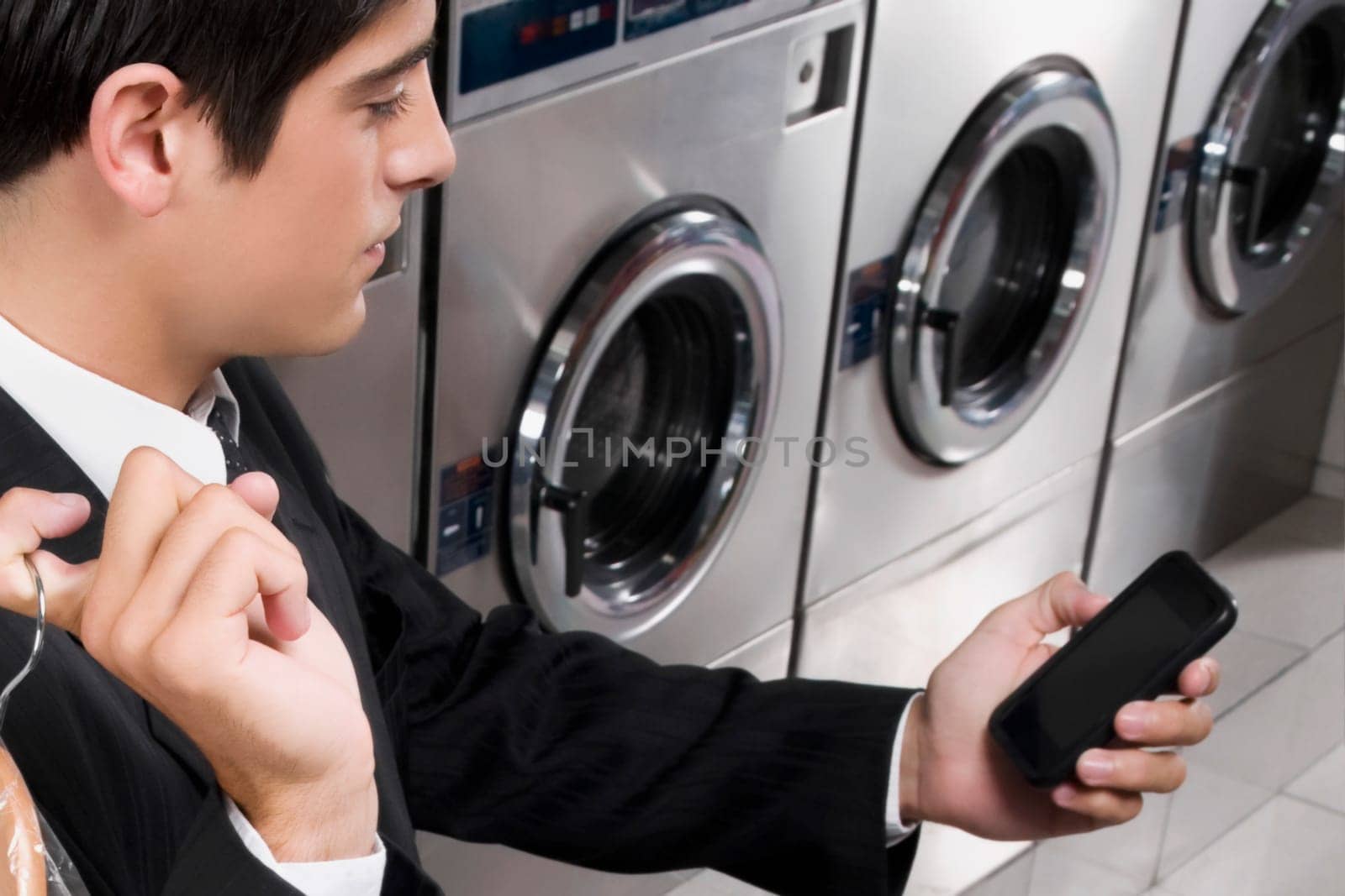 Businessman text messaging on a mobile phone in a laundromat