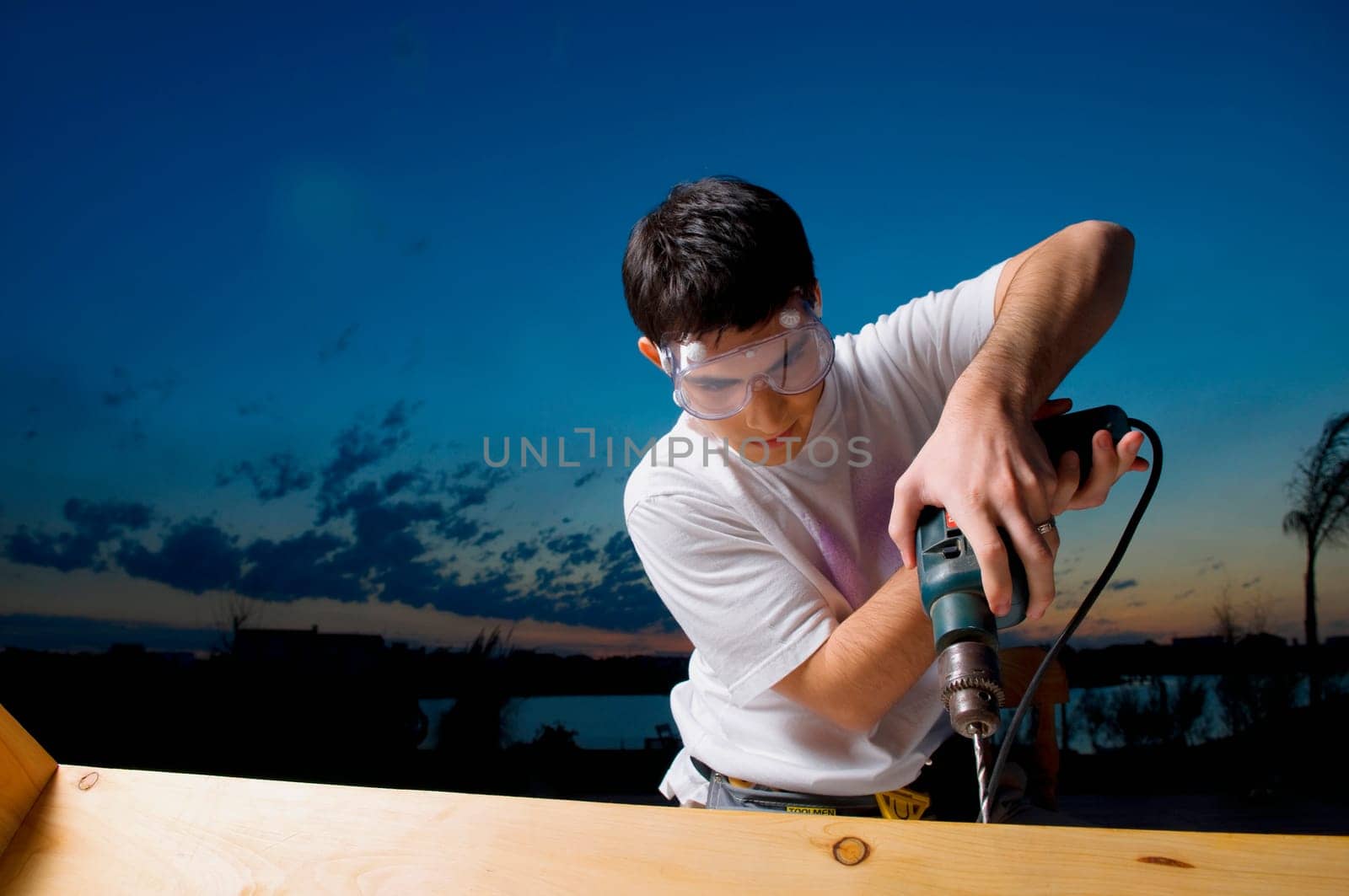 Young man drilling a wooden plank