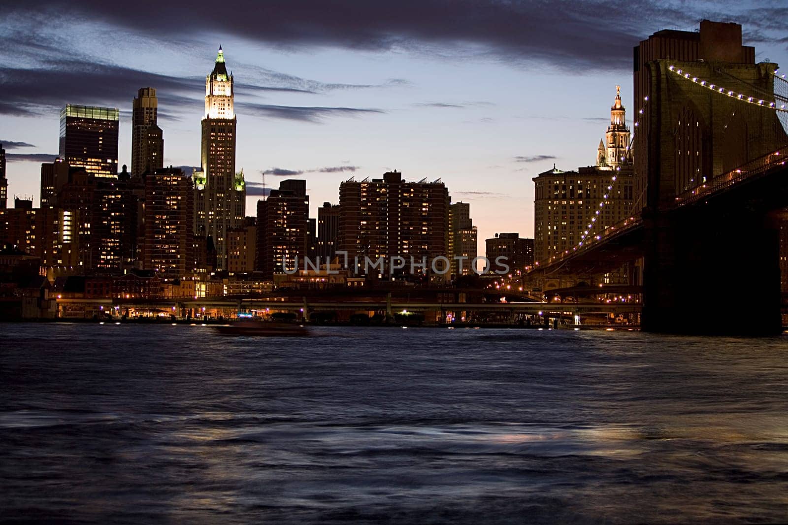 Bridge across a river with buildings lit up in the background at dusk, Brooklyn Bridge, East River, Manhattan, New York City, New York State, USA