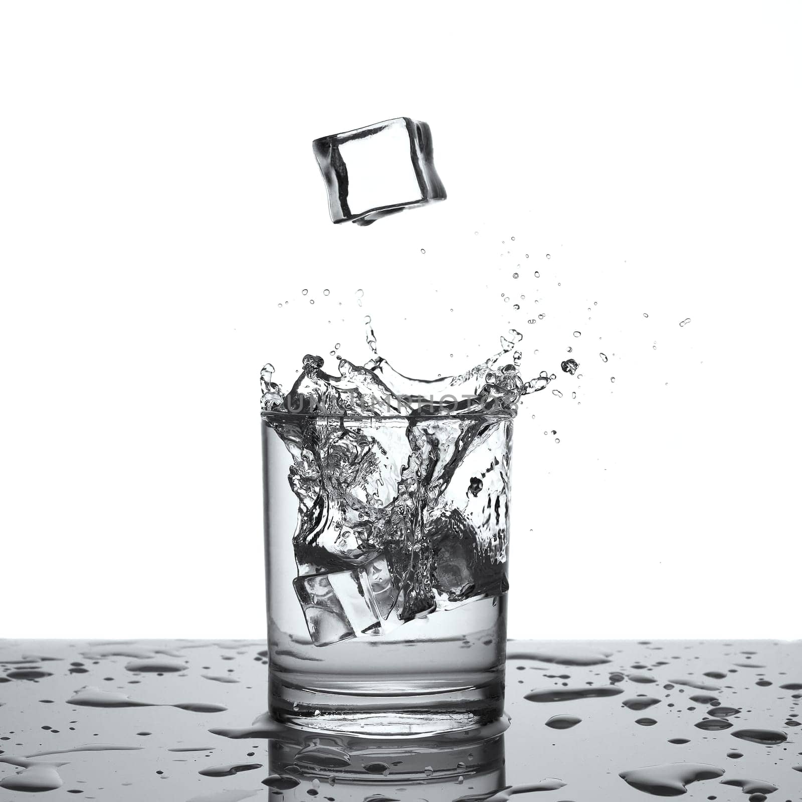 Splashing water. Glass with water or alcohol with splashes from falling ice cubes isolated on white background
