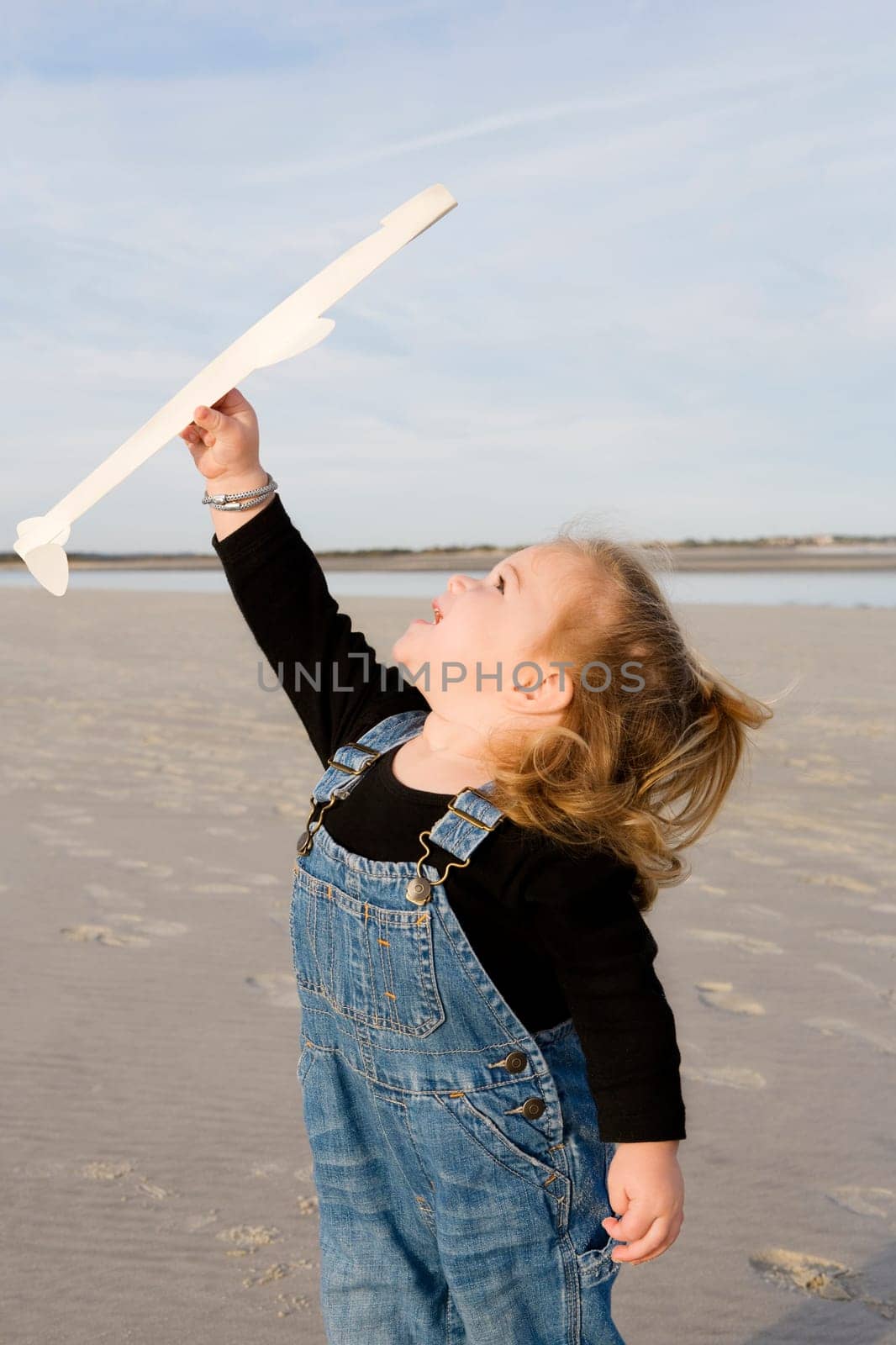 Baby girl playing with a model airplane on the beach