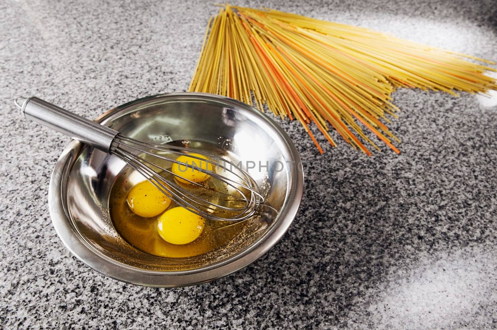 Egg yolk and an egg beater in a bowl with spaghetti