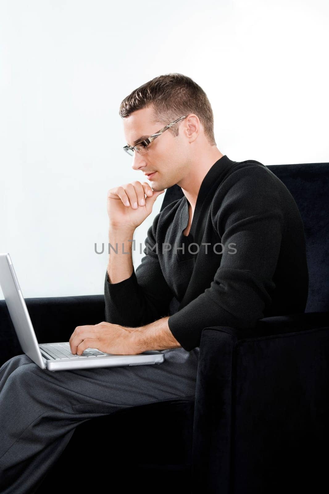 Side profile of a young man sitting in an armchair and working on a laptop