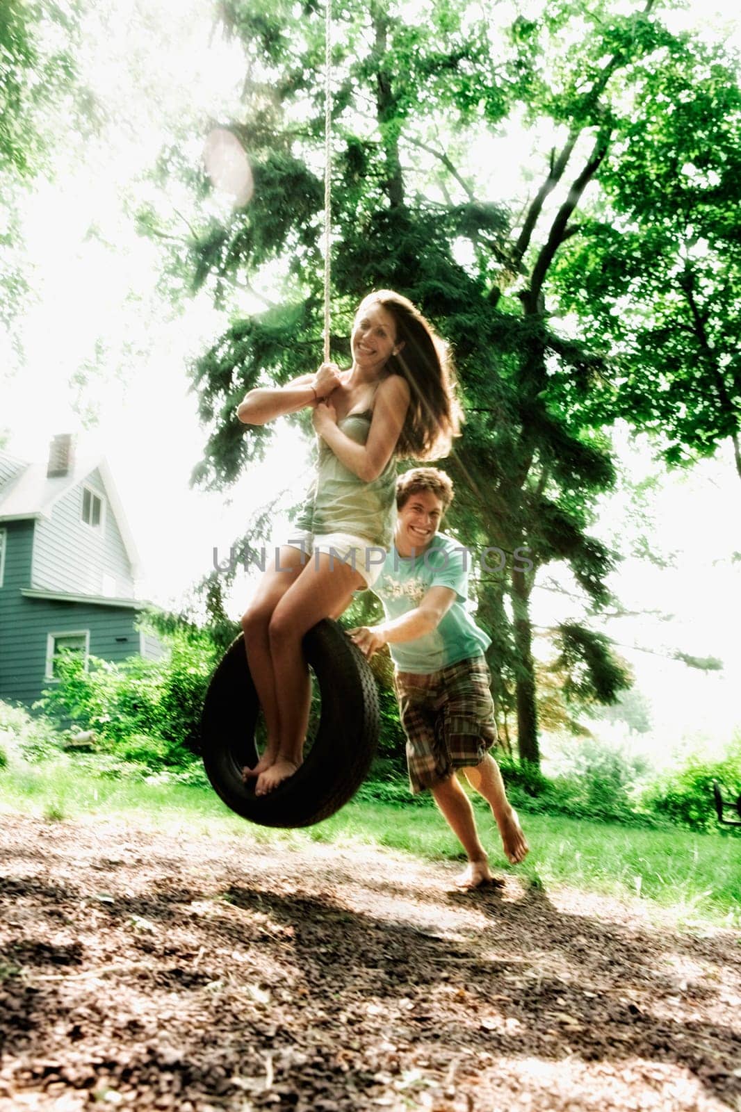 Teenage girl swinging on a tire swing with a young man pushing her