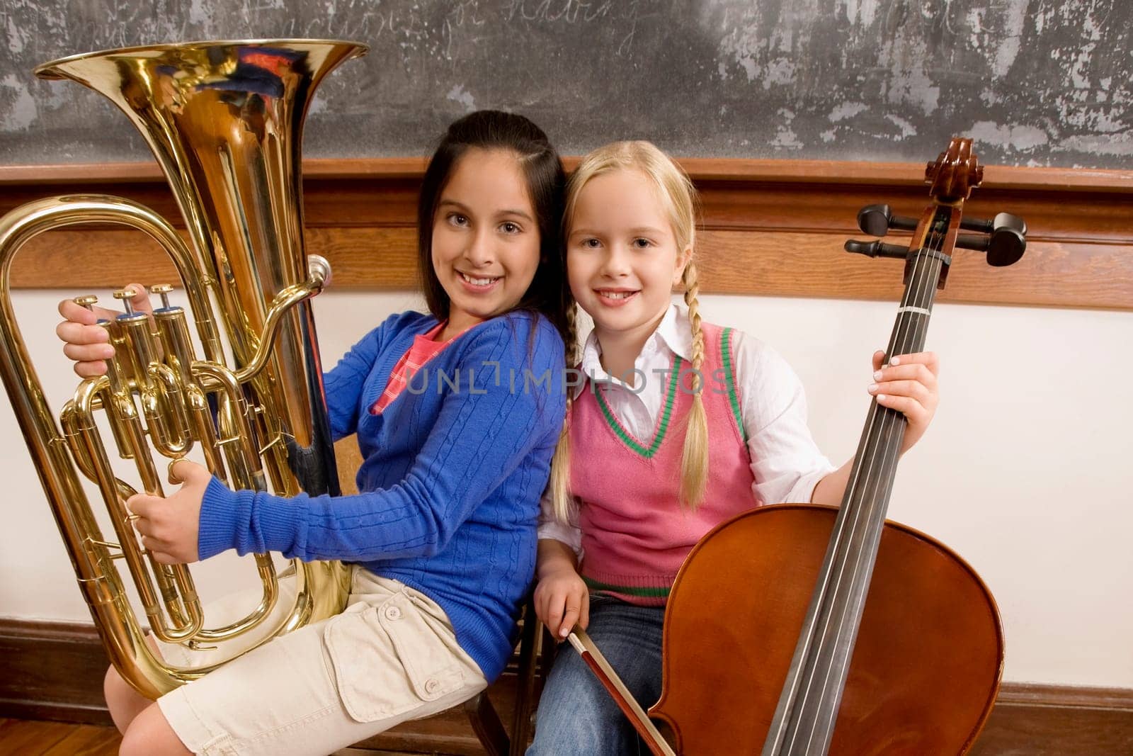 Two schoolgirls playing a cello and a tuba in a classroom