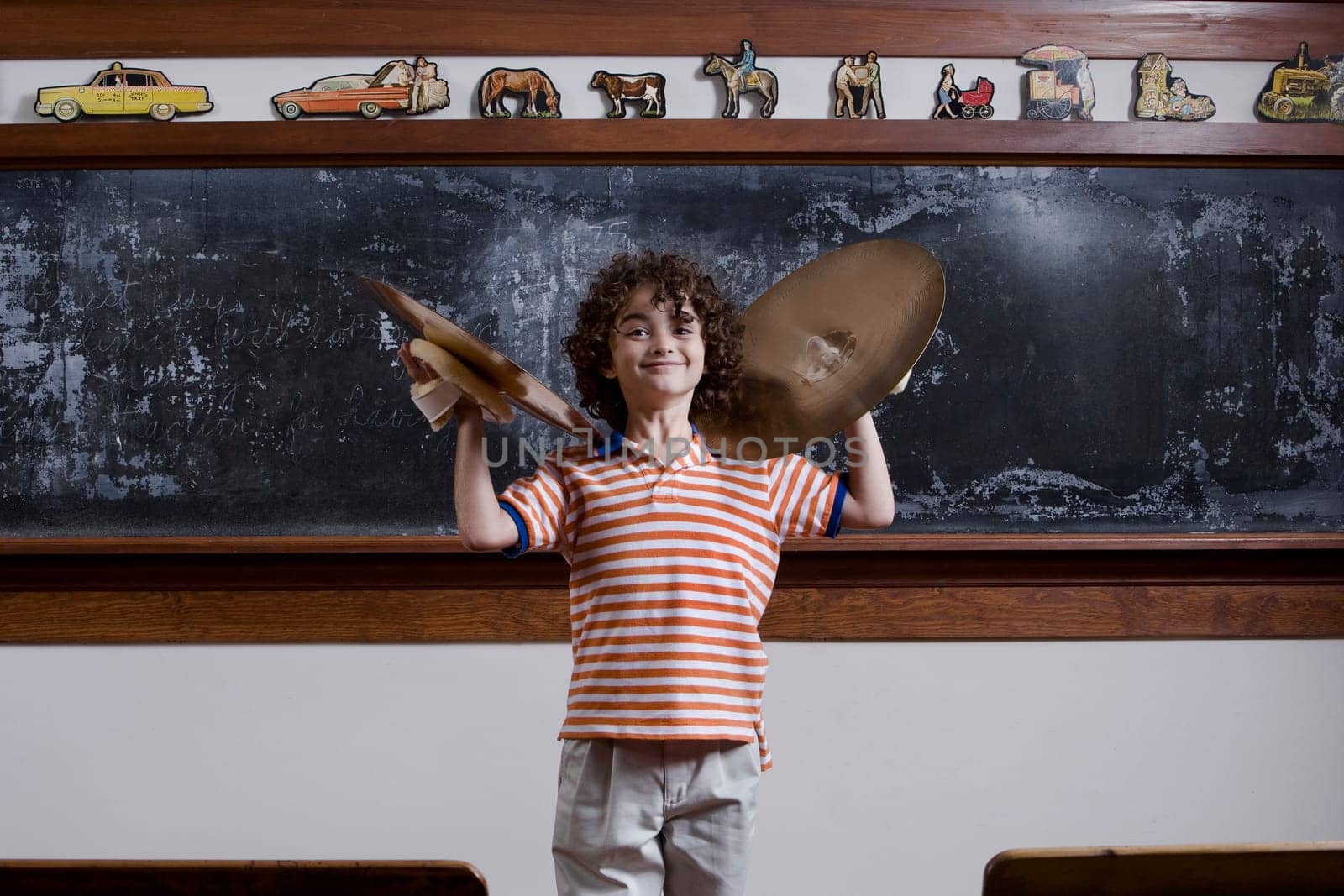 Schoolboy playing cymbals in front of a blackboard