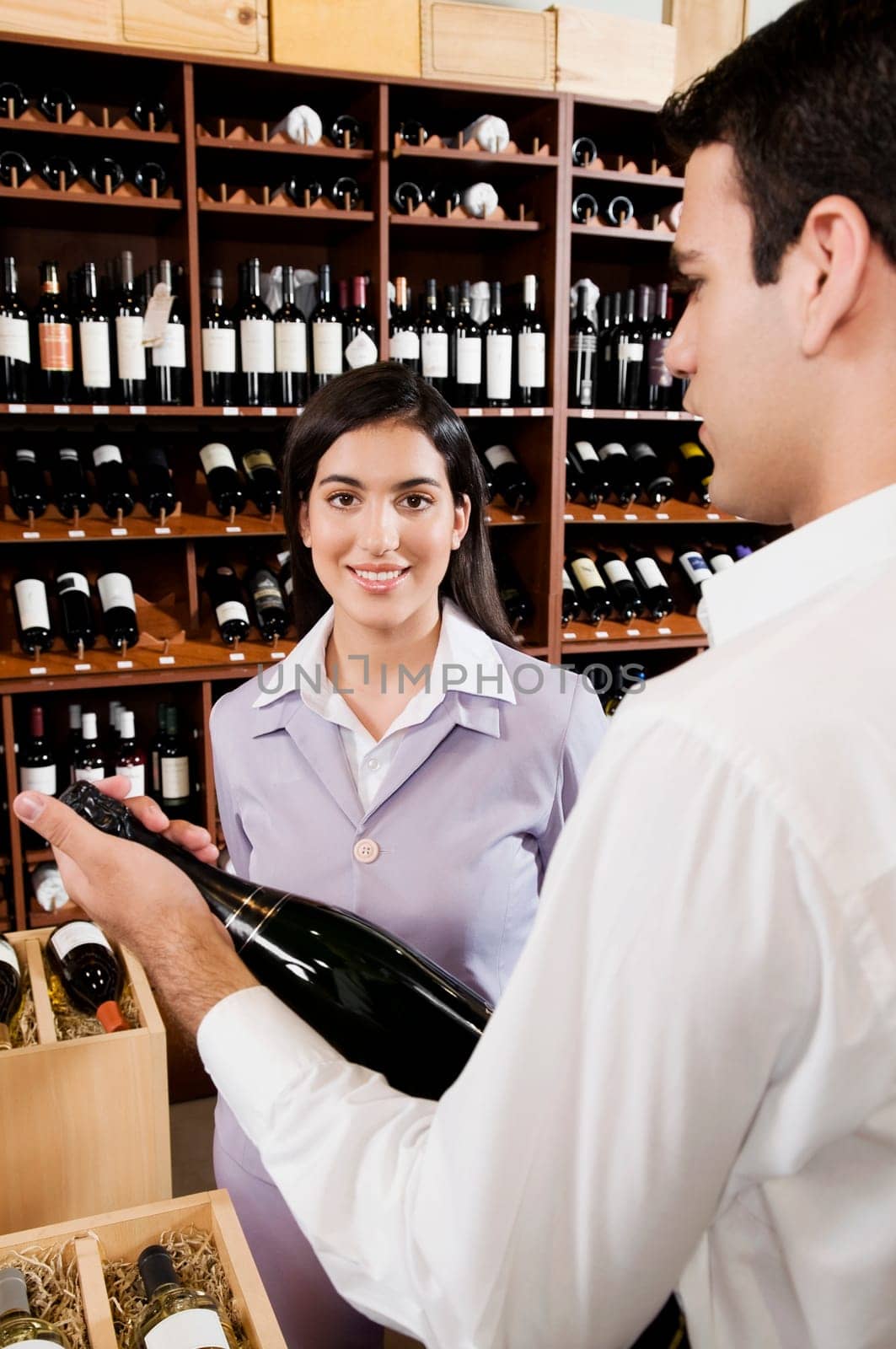 Sales clerk holding a wine bottle beside a businesswoman smiling