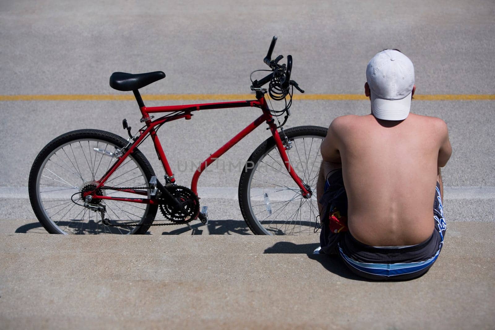 Rear view of a man sitting at roadside with a bicycle, Oak Street Beach, 1000 North Lake Shore Drive, Chicago, Illinois, USA
