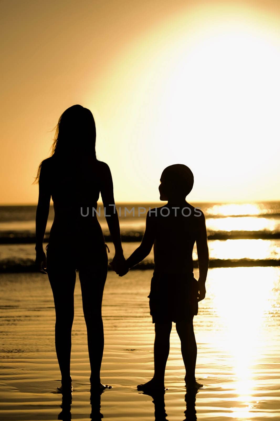 Silhouette of a woman with her son standing on the beach